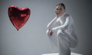 Kobieta w białym stroju siedzi na kostce, opierając głowę na dłoni. Obok niej unosi się czerwone serce-balon. Czy to symbol miłości, czy może zespół Otella?