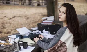 Młoda kobieta, podmiot liryczny, pisze na maszynie w otoczeniu jesiennej przyrody, otoczona notatkami i kawą.