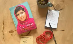 Książka "To ja, Malala", notatnik z cytatem "One child, one teacher, one book, one pen can change the world. Malala", filiżanka herbaty i bransoletki.