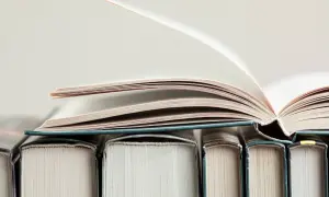 Otwarta księga na stosie innych książek. Kto to jest autor książki?