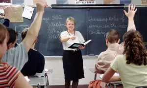 Nauczycielka w klasie, wskazując na tablicę, gdzie uczniowie podnoszą ręce. To praca u podstaw edukacji, budowanie przyszłości.
