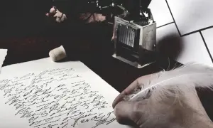 Dłoń z piórem pochyla się nad papierem z odręcznym pismem. Obok leży stempel, jakby czekał na zakończenie tej fraszki.