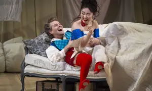 Figaro i jego towarzyszka śmieją się na kanapie, otoczeni pościelą i walizkami.