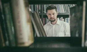 Mężczyzna w białej koszuli, otoczony książkami, przypomina postać z powieści Remigiusza Mroza. Może to być jego rodzeństwo, które również kocha czytać.