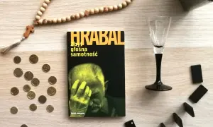 Książka Bohumila Hrabala "Zbyt głośna samotność", paciorki różańca, monety i kostki do gry na drewnianym blacie.