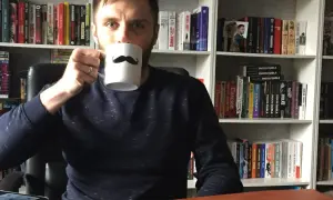 Adrian Bednarek z kubkiem w ręku, otoczony przez półki pełne książek.