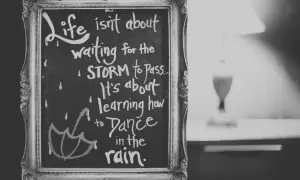Czarno-biała tablica w ozdobnej ramie z inspirującymi cytatami po angielsku: "Life isn't about waiting for the storm to pass. It's about learning how to dance in the rain.