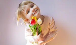 Mała dziewczynka z bukietem tulipanów, jak z wiersza o mamie Szymborska, uśmiecha się do aparatu.