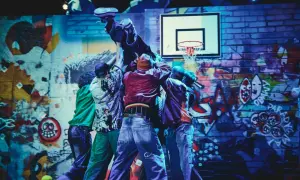 Tancerze w stylu hip-hop unoszą kolegę na tle ściany z graffiti, przypominającej motywy z Ferdydurke.