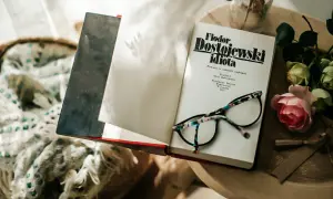 Okładka książki "Fiodor Dostojewski idiota" leży otwarta obok okularów i róży.