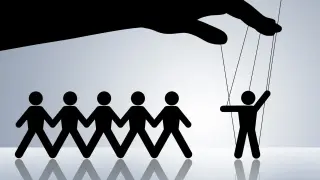 Czarna dłoń steruje ludzikami jak marionetkami. Jedna postać stoi z boku, podniesiona, symbolizując manipulację.