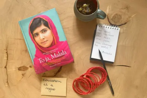Książka "To ja, Malala", notatnik z cytatem "One child, one teacher, one book, one pen can change the world. Malala", filiżanka herbaty i bransoletki.