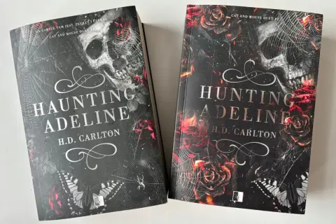 Dwie książki "Haunting Adeline" i "Hunting Adeline" H.D. Carlton. Mroczne okładki z czaszką, różami i pajęczyną.