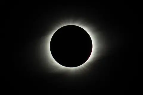 Całkowite zaćmienie Słońca. Czarny dysk Księżyca otoczony jest rozbłyskującą koroną słoneczną, tworząc zjawisko przypominające czarne słońce.