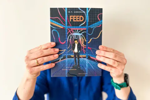 Okładka książki "Feed" M.T. Andersona, przedstawiająca chłopaka w futurystycznym otoczeniu, sugeruje mroczną dystopię.