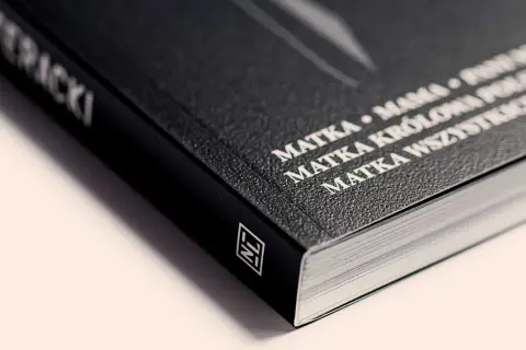 Czarny grzbiet książki z białym napisem "MATKA KRÓLOWA WSZYSTKICH SZCZĘŚLIWYCH". Ten artykuł to prawdziwe dzieło sztuki.