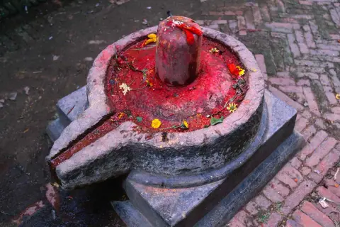 Kamienna podstawa z rynienką, na niej czerwony, ozdobiony kwiatami lingam, symbolizujący boga Śiwę.