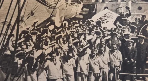Marynarze na pokładzie statku "Dar Pomorza" w Gdyni. W tle widać żagle i maszty, a na pierwszym planie grupę ludzi w białych strojach. To jakby smuga cienia autorstwa historii.