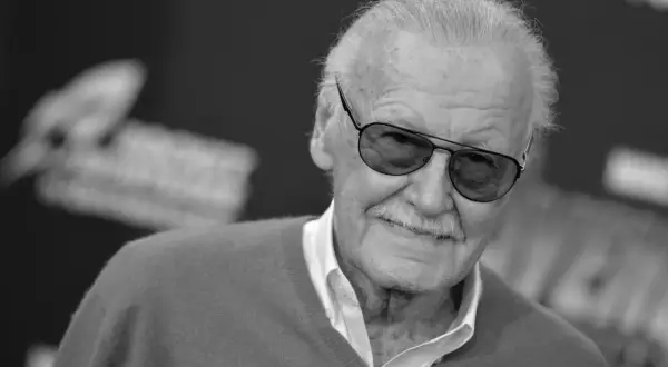 Uśmiechnięty Stan Lee Marvel w okularach przeciwsłonecznych, z siwymi włosami i charakterystycznymi wąsami.