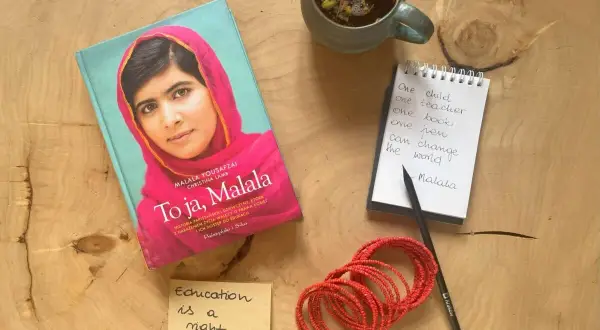 Książka "To ja, Malala", notatnik z cytatem "One child, one teacher, one book, one pen can change the world. Malala", filiżanka herbaty i bransoletki.