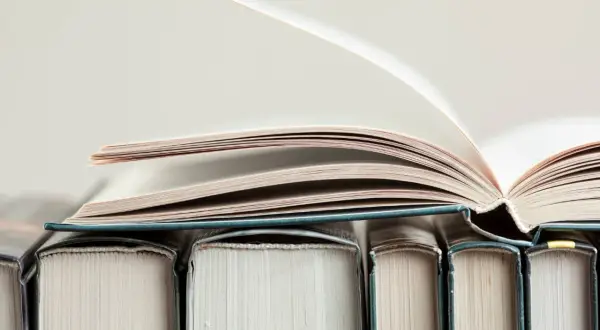 Otwarta księga na stosie innych książek. Kto to jest autor książki?