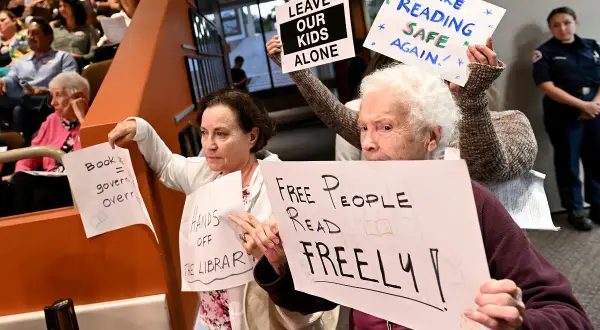 Protest przeciwko cenzurze w bibliotece. Ludzie trzymają transparenty: "Wolni ludzie czytają swobodnie", "Zostawcie nasze dzieci w spokoju", "Uczyńmy czytanie znów bezpiecznym".