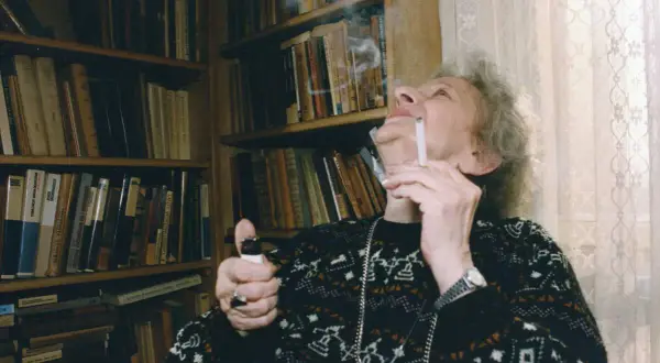 Wisława Szymborska, zapalając papierosa, otoczona książkami. Ciekawe, o czym myślała?