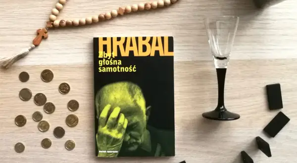 Książka Bohumila Hrabala "Zbyt głośna samotność", paciorki różańca, monety i kostki do gry na drewnianym blacie.
