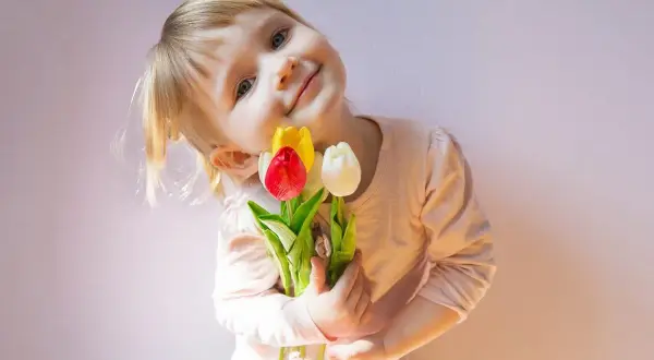 Mała dziewczynka z bukietem tulipanów, jak z wiersza o mamie Szymborska, uśmiecha się do aparatu.