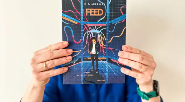 Okładka książki "Feed" M.T. Andersona, przedstawiająca chłopaka w futurystycznym otoczeniu, sugeruje mroczną dystopię.