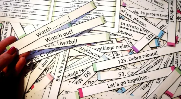Stos kartek z angielskim tekstem do nauki. Widać fragmenty zdań, np. "Watch out!", "Let's go together.", "125. Dobra robota!".
