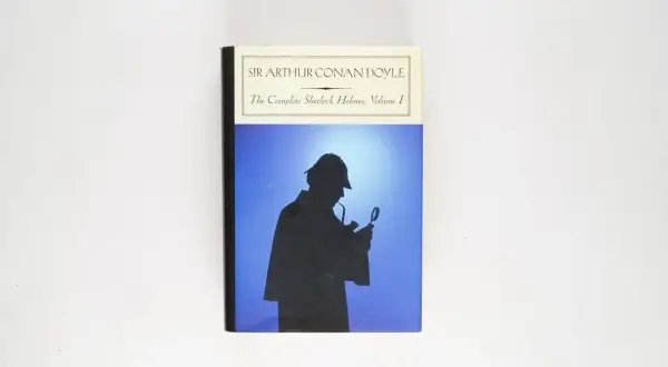 Okładka "The Complete Sherlock Holmes, Volume I" Sir Arthura Conana Doyle'a. Sylwetka detektywa z lupą i fajką na tle błękitnego nieba.