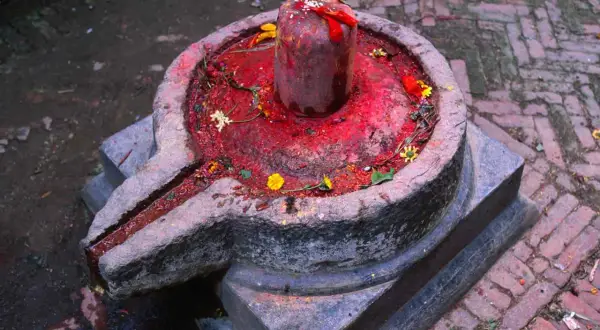 Kamienna podstawa z rynienką, na niej czerwony, ozdobiony kwiatami lingam, symbolizujący boga Śiwę.
