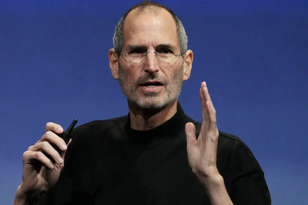 Steve Jobs, w okularach i czarnym golfie, trzyma w dłoni mały przedmiot. Ciekawe fakty o jego życiu i karierze.