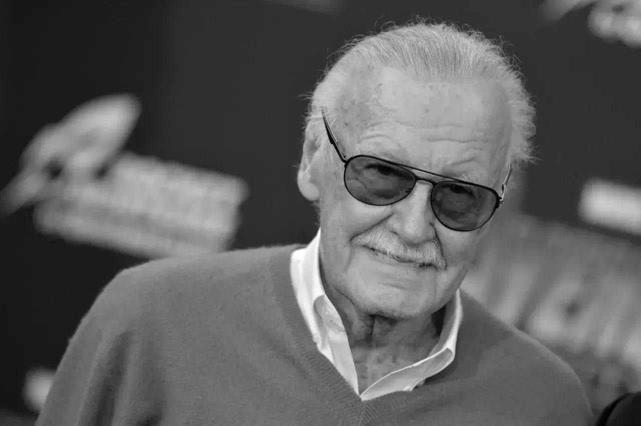 Uśmiechnięty Stan Lee Marvel w okularach przeciwsłonecznych, z siwymi włosami i charakterystycznymi wąsami.
