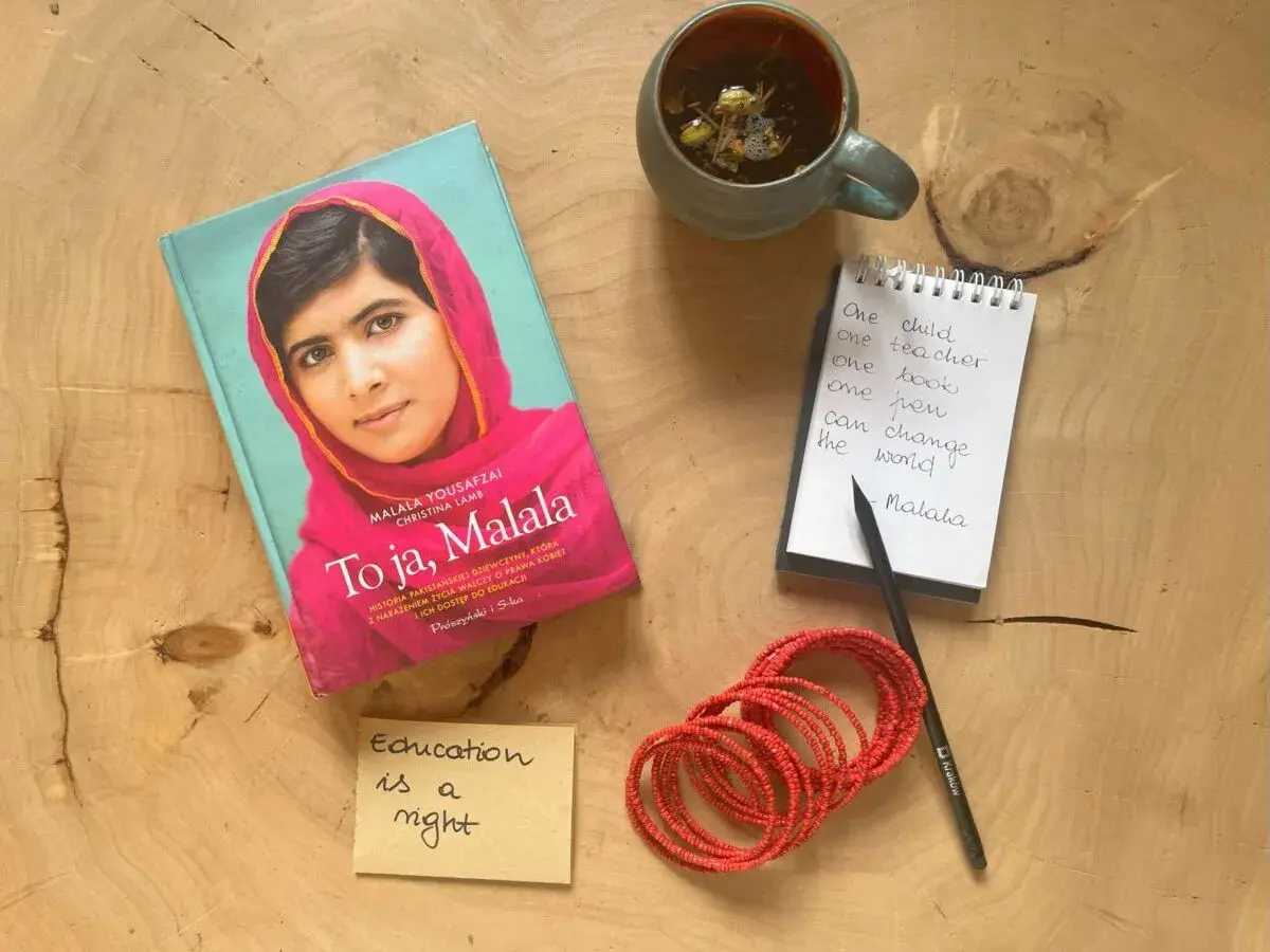 Książka "To ja, Malala", notatnik z cytatem "One child, one teacher, one book, one pen can change the world. Malala", filiżanka herbaty i bransoletki.