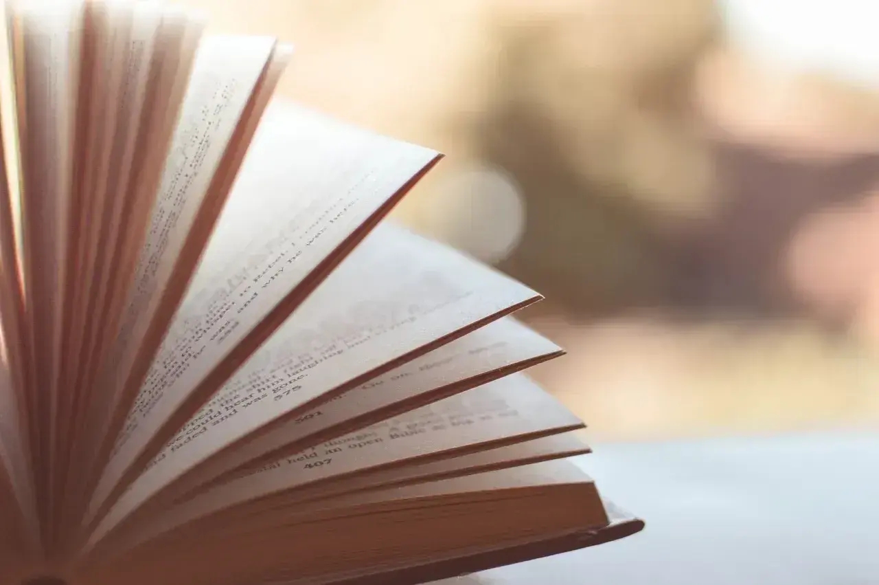 Otwarta książka, strony falują, ukazując tekst. To jak synkretyzm w literaturze, gdzie różne wątki splatają się w jedną opowieść.