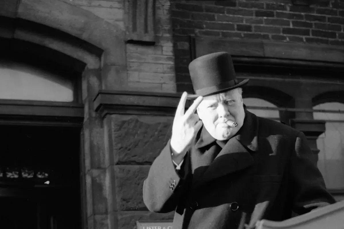 Winston Churchill z cygarem i kapeluszem, pokazujący znak zwycięstwa. Ciekawostki o nim często dotyczą jego charyzmy.