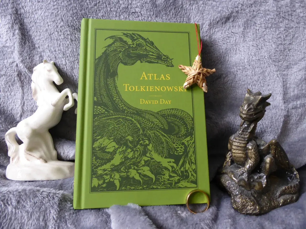 Zielona okładka "Atlasu Tolkienowskiego" z wizerunkiem smoka, obok figurka konia i smoka, oraz pierścień. To wszystko, co napisał Tolkien, w jednym miejscu.
