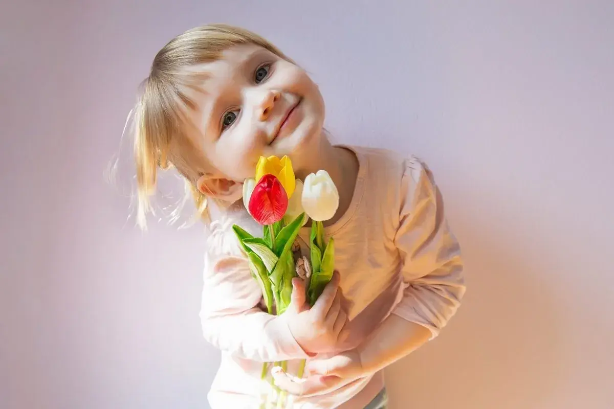 Mała dziewczynka z bukietem tulipanów, jak z wiersza o mamie Szymborska, uśmiecha się do aparatu.