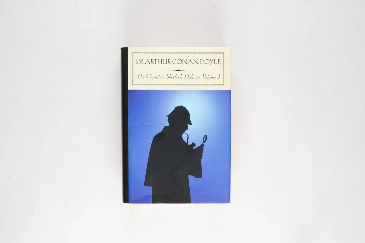 Okładka "The Complete Sherlock Holmes, Volume I" Sir Arthura Conana Doyle'a. Sylwetka detektywa z lupą i fajką na tle błękitnego nieba.