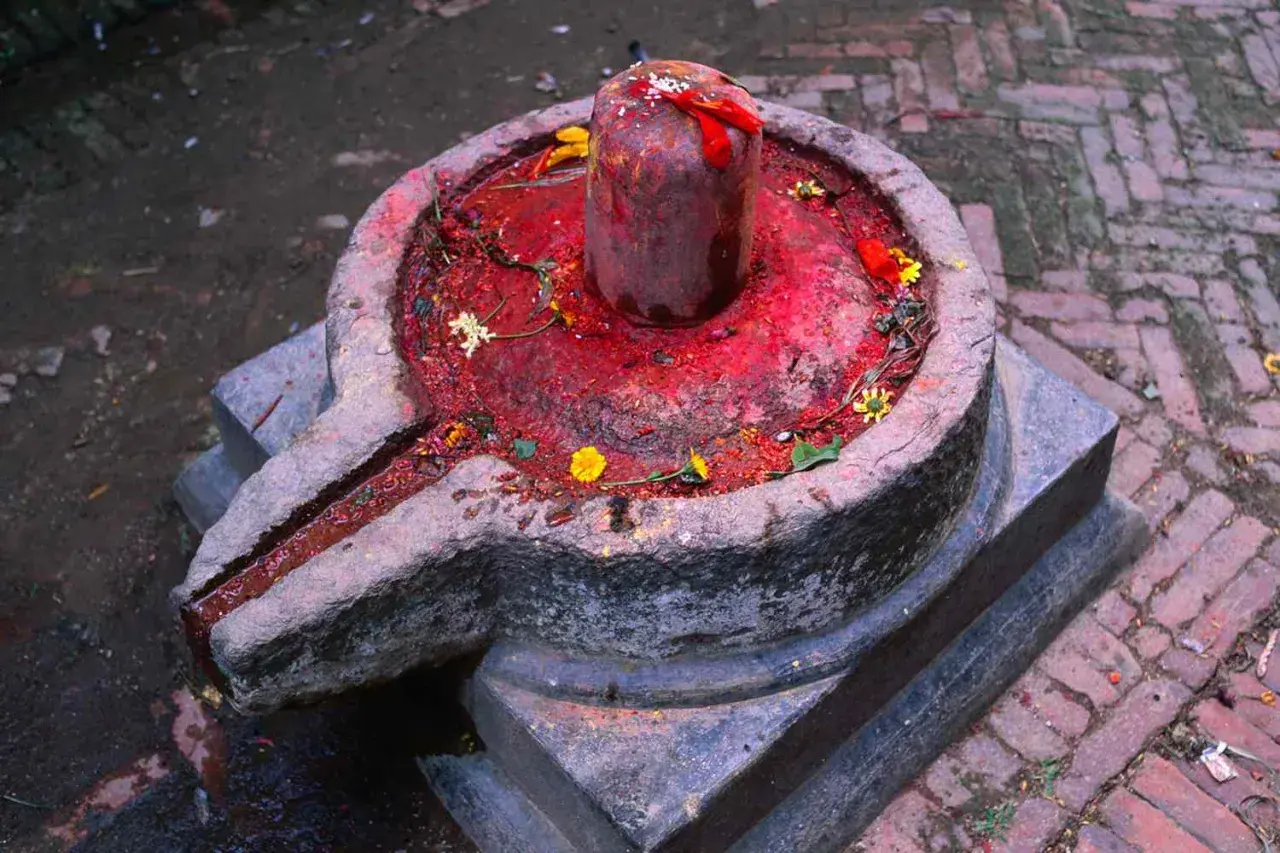 Kamienna podstawa z rynienką, na niej czerwony, ozdobiony kwiatami lingam, symbolizujący boga Śiwę.