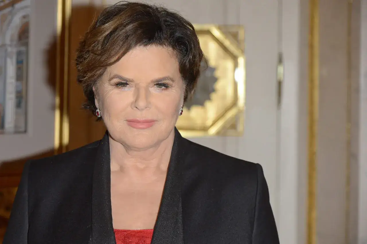 Alicja Resich Modlińska w eleganckiej czarnej marynarce i czerwonej sukience, z błyszczącymi kolczykami.