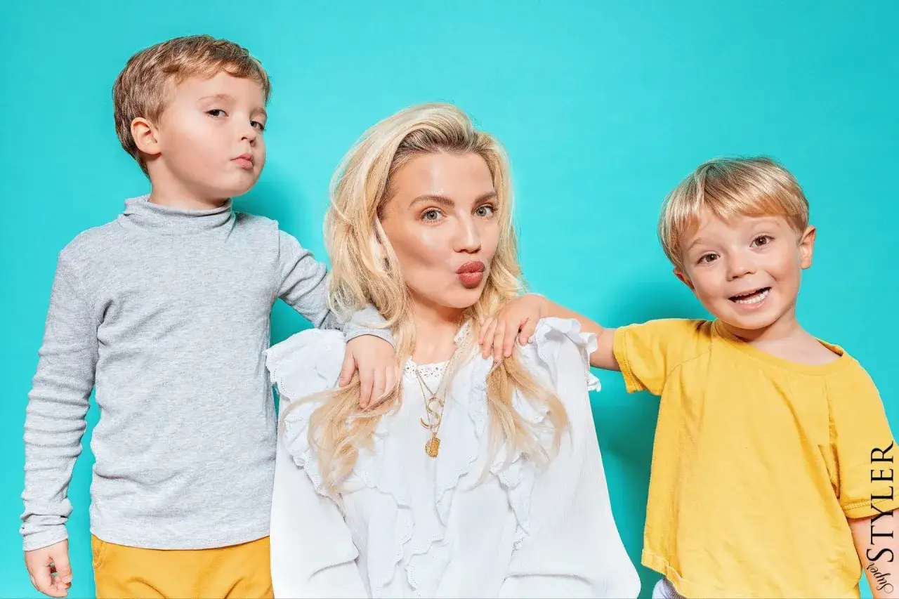 Mama z synami, jak z najlepszych cytatów o mamie. Jeden syn z miną, drugi uśmiechnięty, a mama całuje.