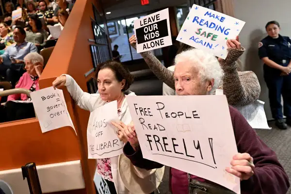 Protest przeciwko cenzurze w bibliotece. Ludzie trzymają transparenty: "Wolni ludzie czytają swobodnie", "Zostawcie nasze dzieci w spokoju", "Uczyńmy czytanie znów bezpiecznym".