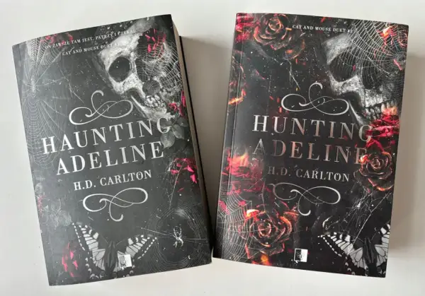 Dwie książki "Haunting Adeline" i "Hunting Adeline" H.D. Carlton. Mroczne okładki z czaszką, różami i pajęczyną.
