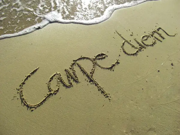 Napis "Carpe diem" na piasku, tuż przy falach. To przypomnienie, co oznacza cytat: chwytaj dzień!