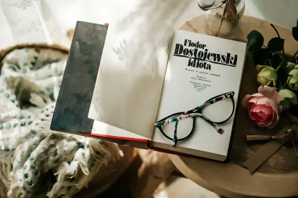 Okładka książki "Fiodor Dostojewski idiota" leży otwarta obok okularów i róży.