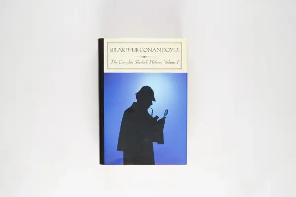 Okładka "The Complete Sherlock Holmes, Volume I" Sir Arthura Conana Doyle'a. Sylwetka detektywa z lupą i fajką na tle błękitnego nieba.
